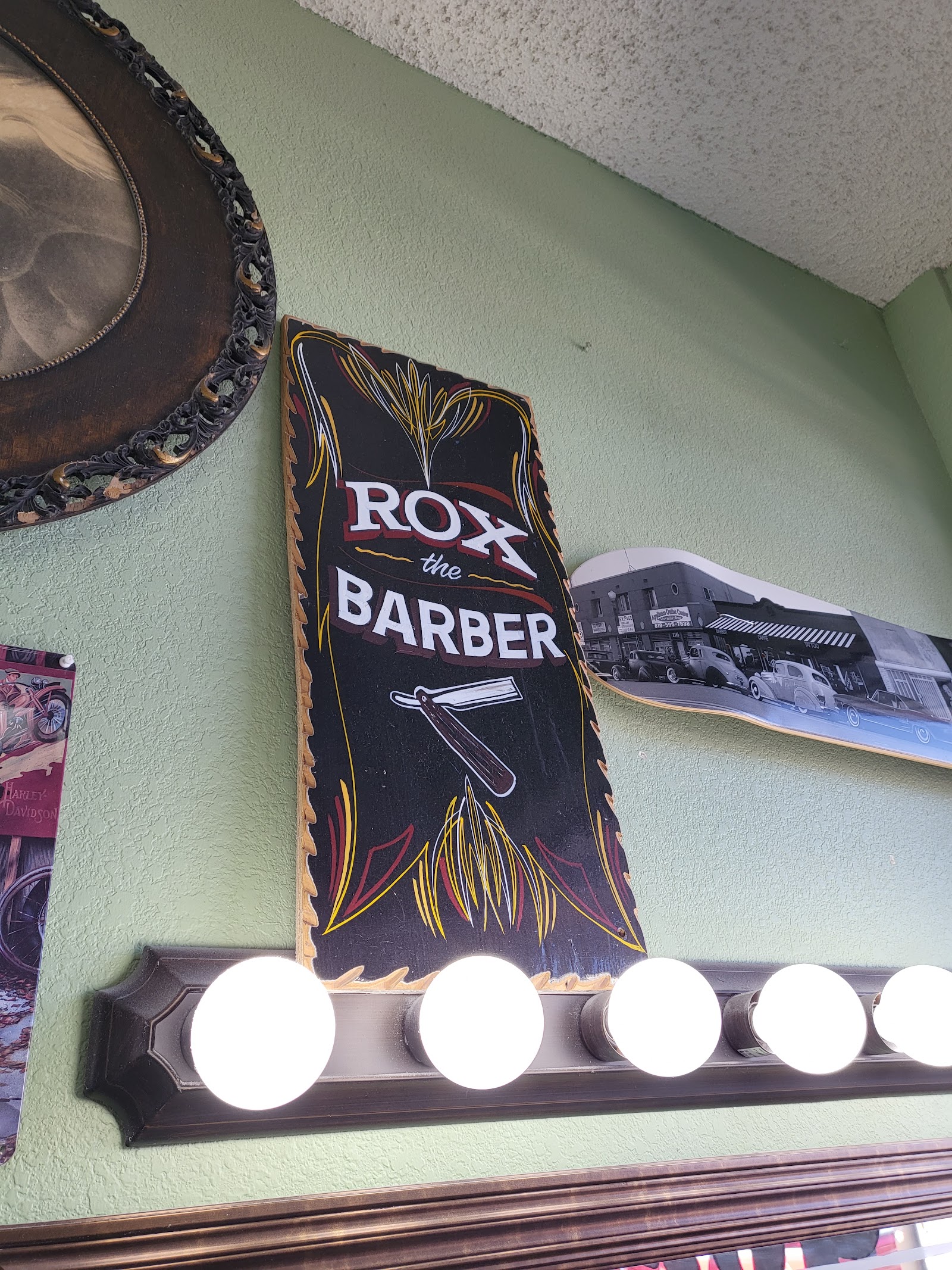 Hand-painted Rox the Barber pinstriped sign on green wall above vanity lights