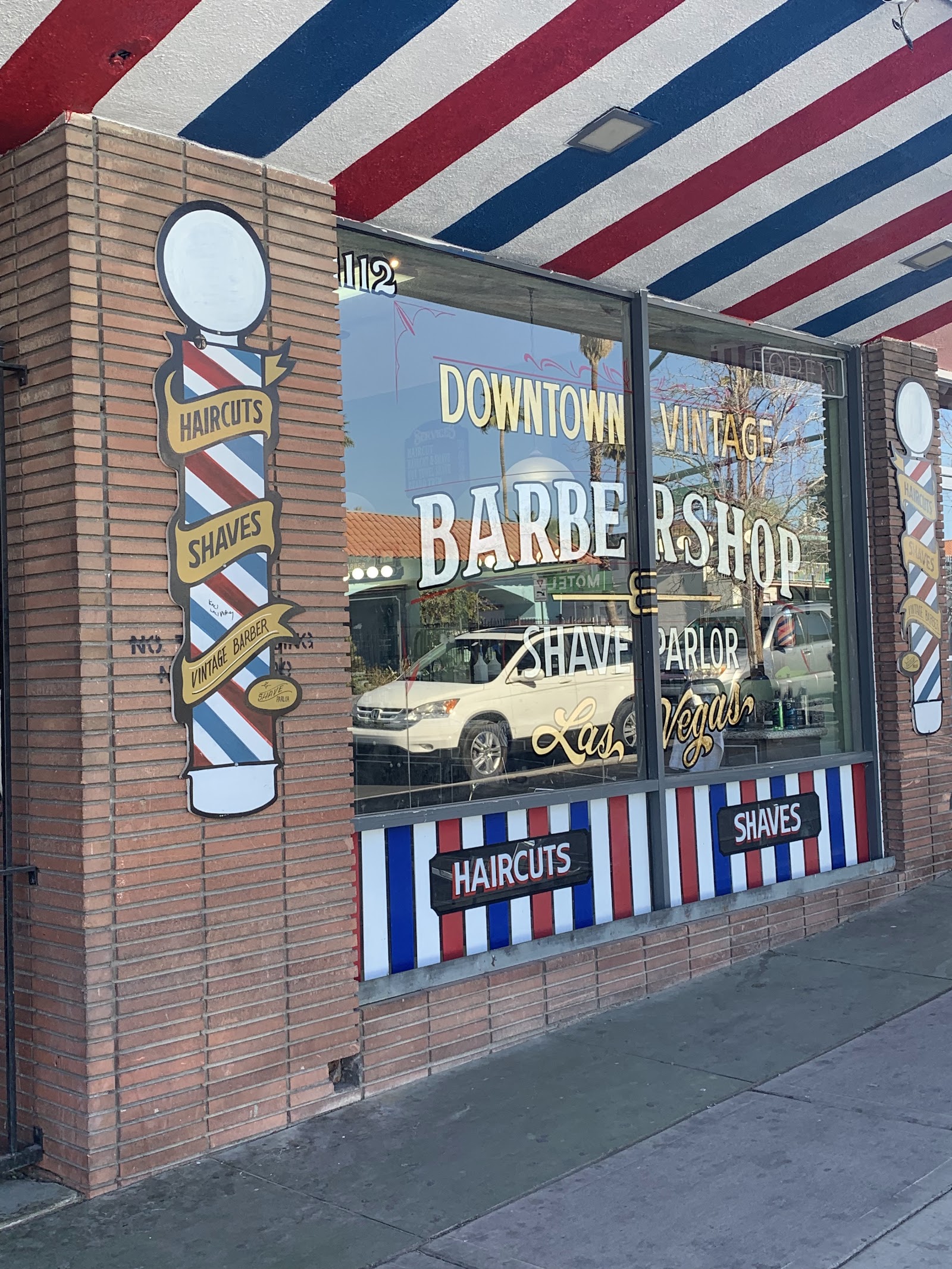 Storefront window reading Downtown Vintage Barbershop Shave Parlor Las Vegas with barber poles and striped awning